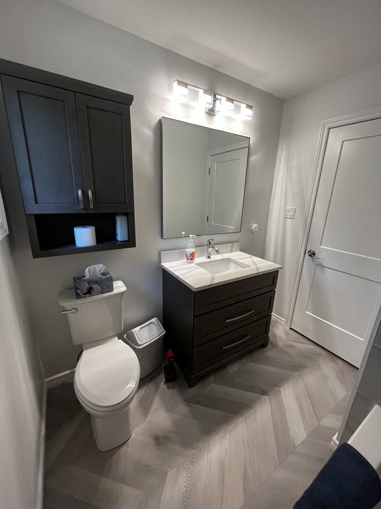A compact bathroom with a glass shower enclosure, white tiled floor, and a modern vanity next to a toilet.