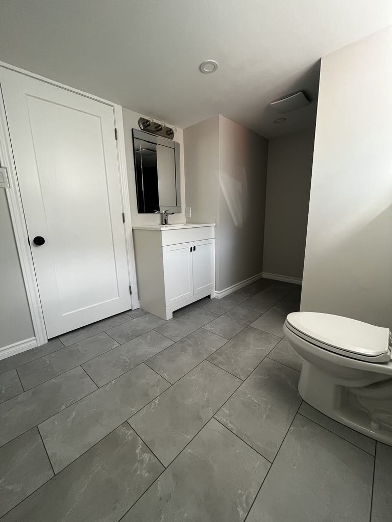 A bright, minimalistic bathroom with a white vanity, gray floor tiles, and plumbing connections for a washer and dryer.