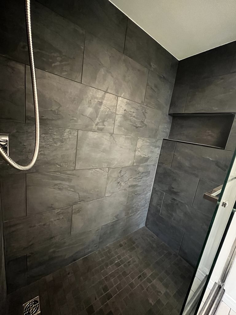 A modern walk-in shower with black textured tiles, a rain shower head, and a handheld shower attachment.