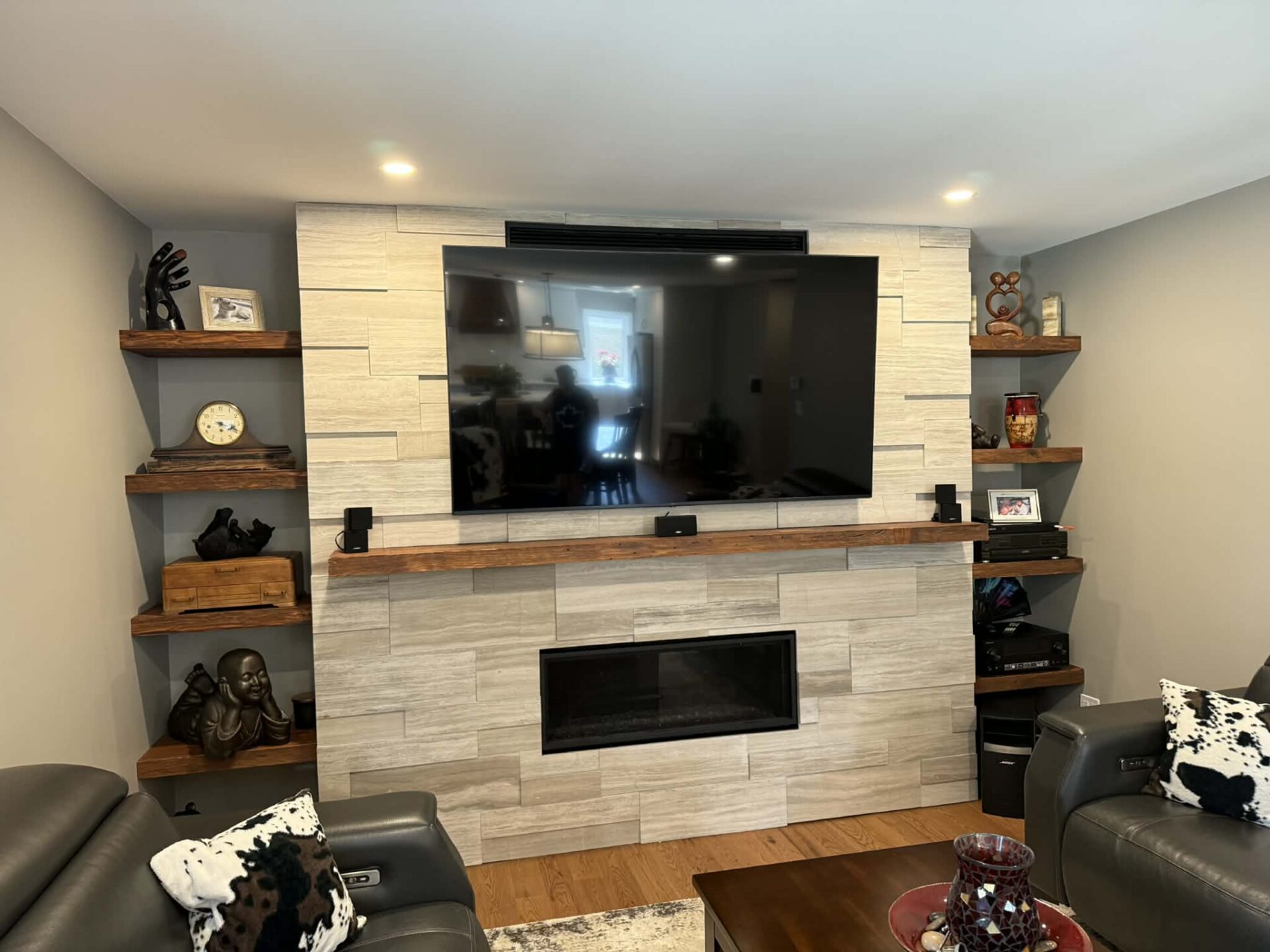 Custom living room feature wall in Cornwall, Ontario with large mounted TV, textured tile surround, linear fireplace, and floating wood shelves, built by JSM Elite Contracting.