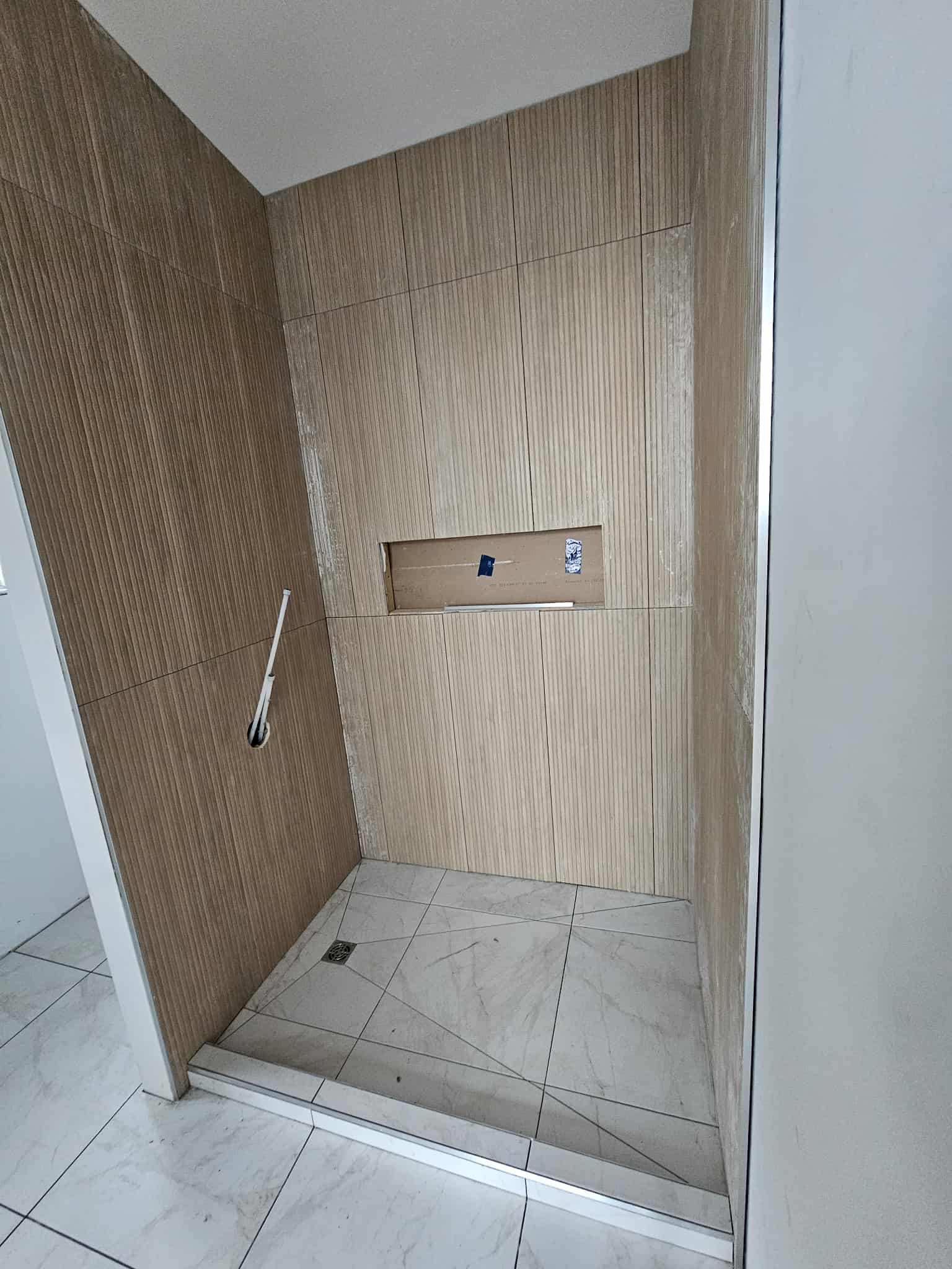 In-progress custom shower installation in Cornwall, Ontario with vertical wood-look wall tiles, marble-look tile floor, recessed shower niche, and low curb by JSM Elite Contracting.