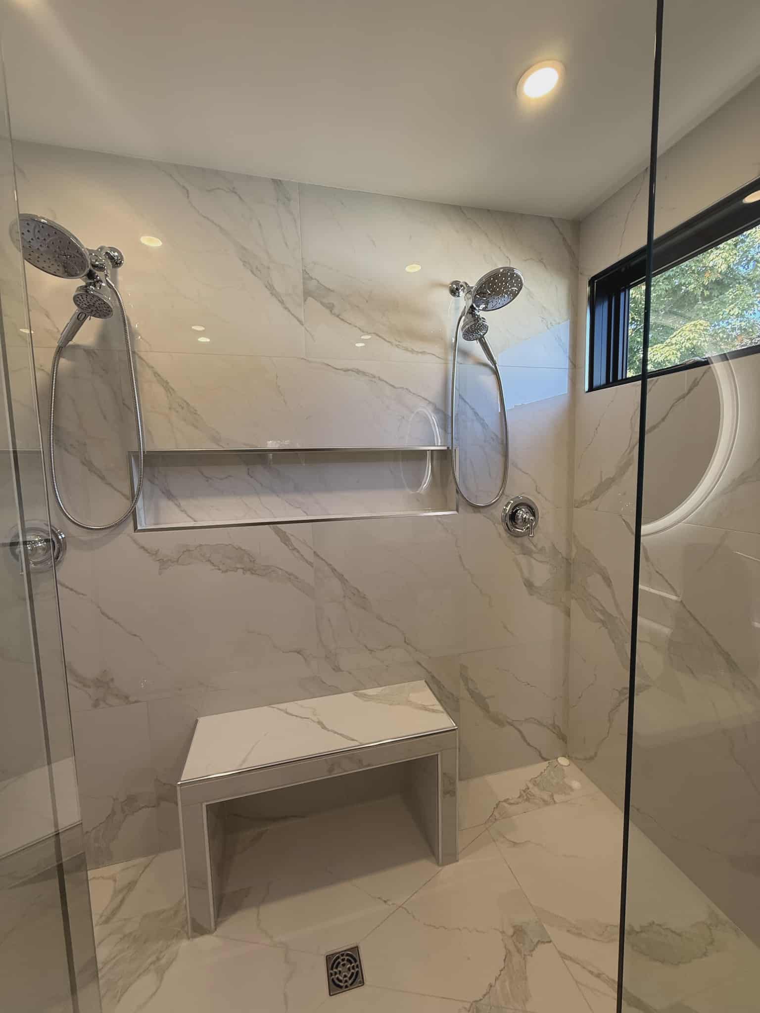 Luxury walk-in shower with custom marble-look bench, dual shower heads, long recessed niche, and frameless glass enclosure, renovated by JSM Elite Contracting in Cornwall, Ontario.