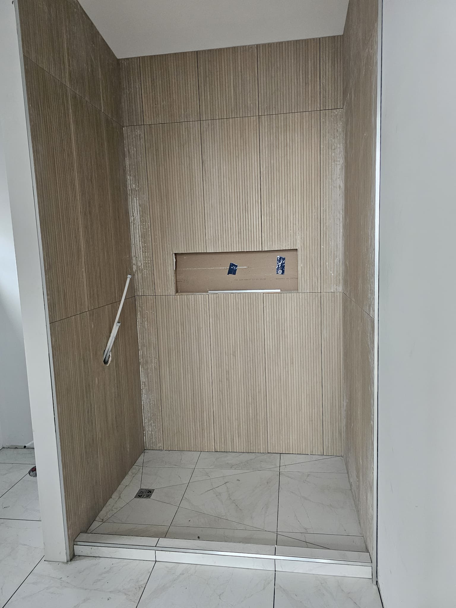 In-progress shower niche installation in a custom walk-in shower with vertical wood-look wall tiles, marble-look floor, and low curb by JSM Elite Contracting in Cornwall, Ontario.